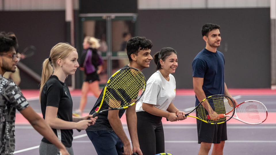 Students in the tennis centre lined up ready to hit a tennis ball, working together as a team.