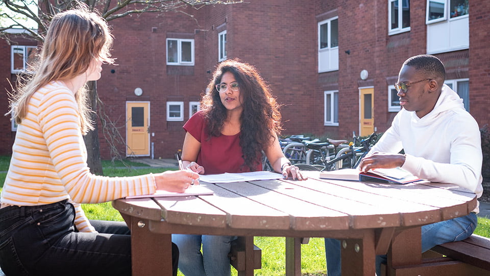 Three postgraduate students sitting at a bench outside a halls of residence