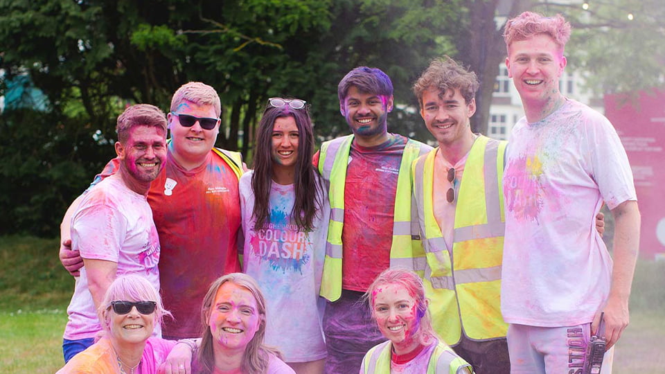 RAG students smiling to the camera and covered in powder paint after throwing a colour run.