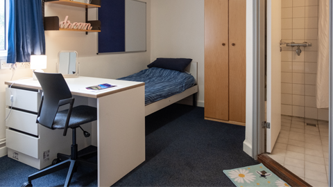 One of the beds in a twin room with a desk at the bottom of the bed