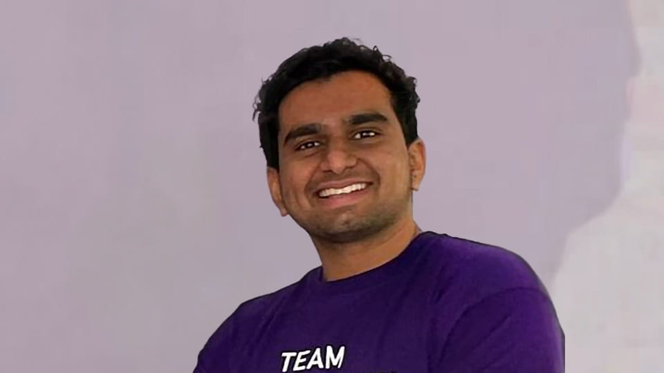 Loughborough Student wears purple welcome to loughborough t-shirt and smiles toward the camera.
