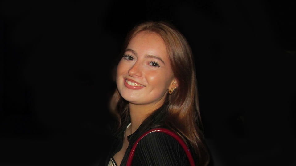 Student is in the middle of a darkened night club and turns to smile to camera.