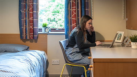 Standard bedroom in Harry French with student sat working at their desk opposite their bed in Loughborough University student accommodation.