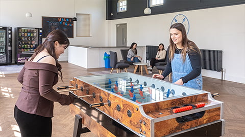 Students laughing together while playing table football in Harry French's recently renovated common room