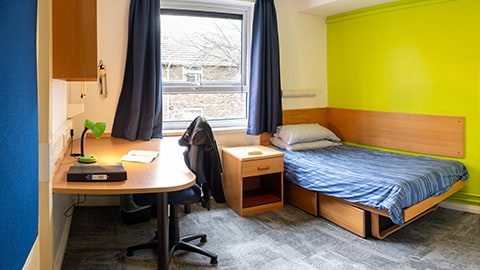 An en-suite bedroom at student accommodation option Rutherford, this room has a large study desk with shelving, a comfy bed and a private bathroom