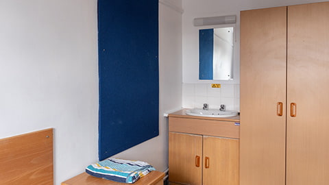 A washbasin, wardrobe and bed-side table in a standard Rutherford bedroom