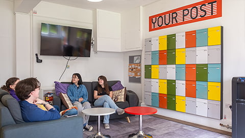 Students in a communal seating area in The Holt reception, next to the postal collection area with brightly coloured post boxes for letters