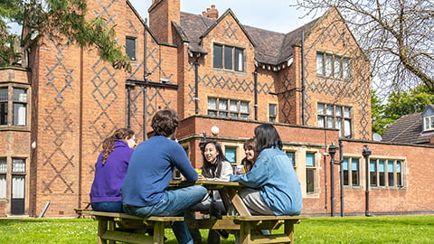Students sitting at a picnic bench outside of the Holt, a gorgeous historic student accommodation choice at Loughborough University