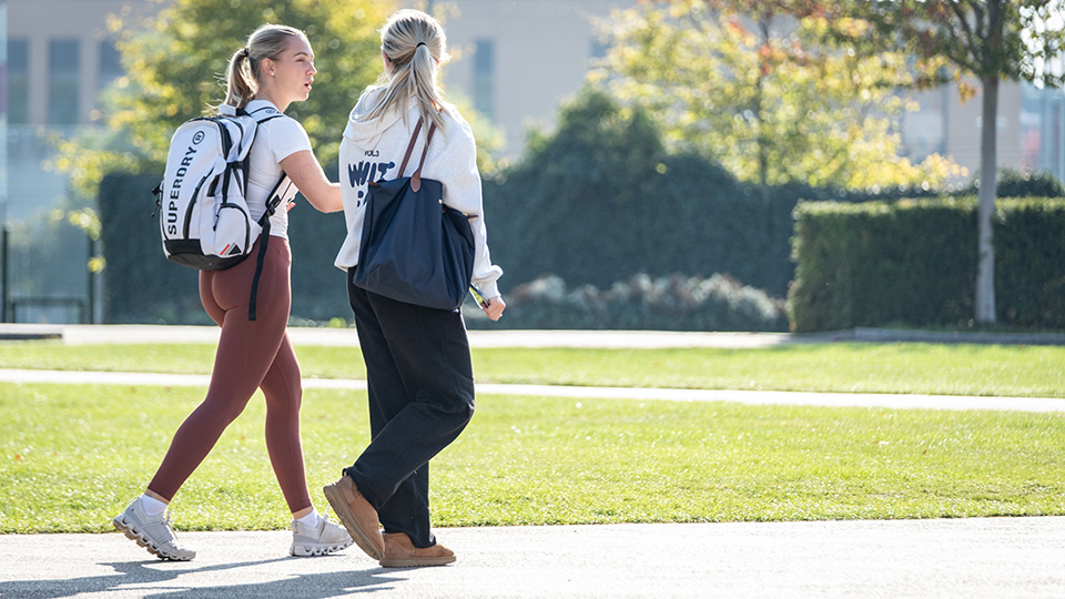 Two students walking across a grassed area
