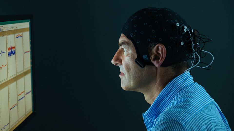 Tony Dawson with monitoring equipment on his head sitting looking at a computer screen