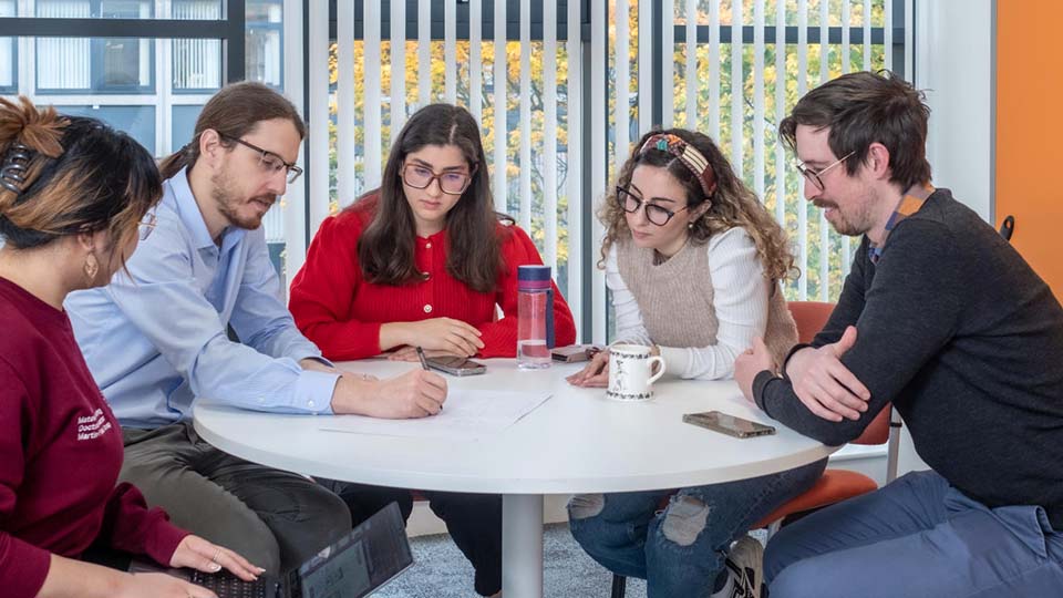 Students in discussion with an academic around a round table.