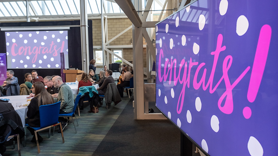 people sitting at tables with large screens displaying congrats