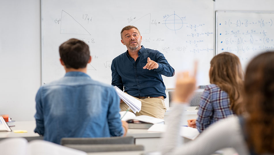 A lecturer holding a lecture, in front of a white blackboard, students with their backs to him listening to his lecture