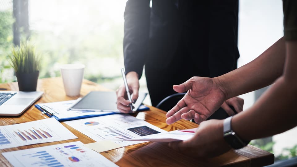 Research papers and laptop on a table with a view of hands using the materials