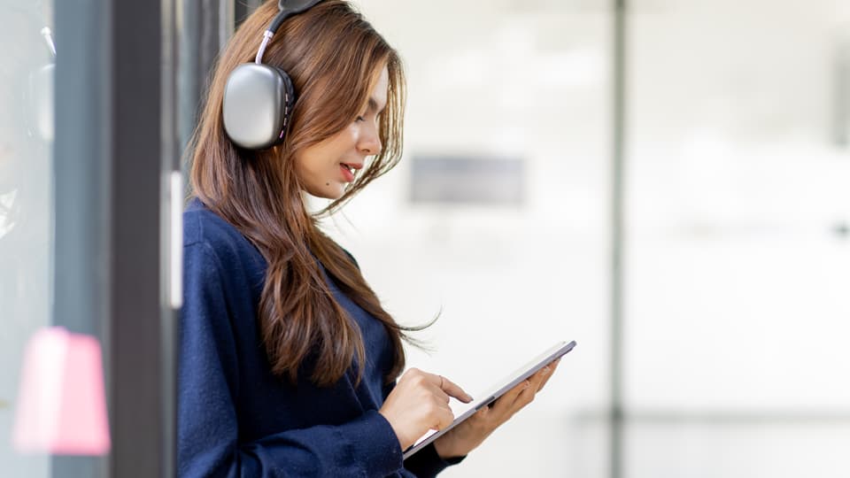 Female student with long red hair wearing headphones and using a tablet computer