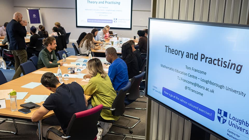 a group of people sitting at desks with a presentation on a screen in the foreground
