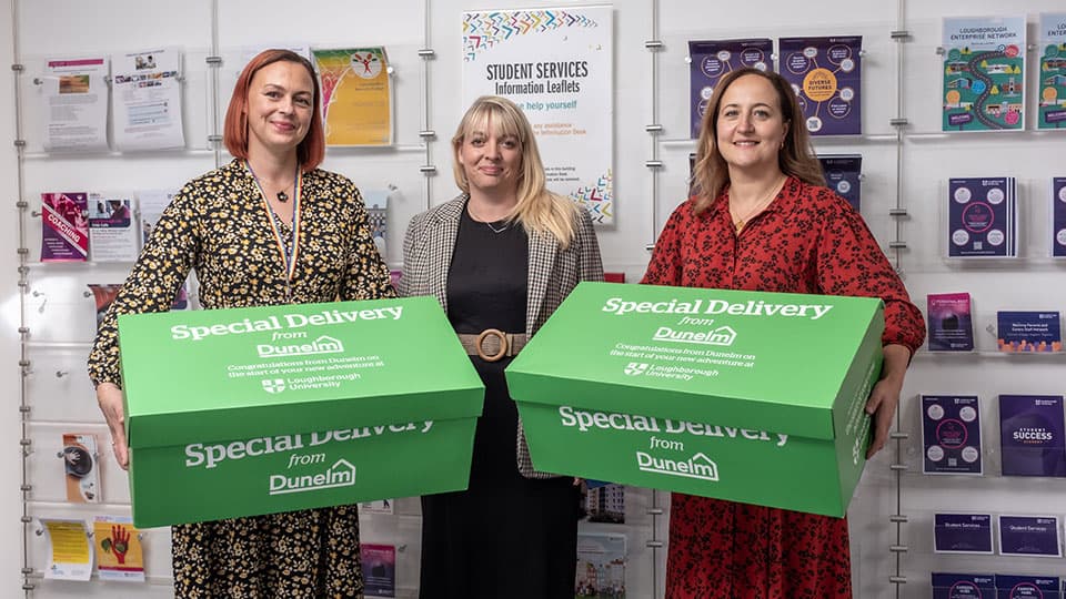 three people standing, two are holding large boxes from Dunelm