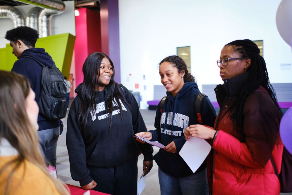 Four people stood in the foyer of a building talking with a fifth person in the background