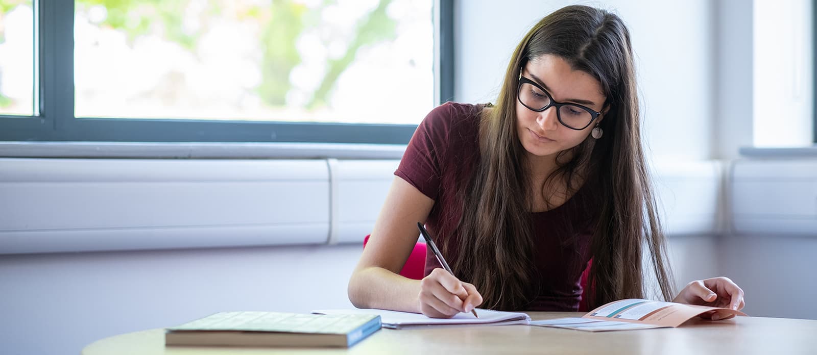 A student sat at a desk, reading a document and writing