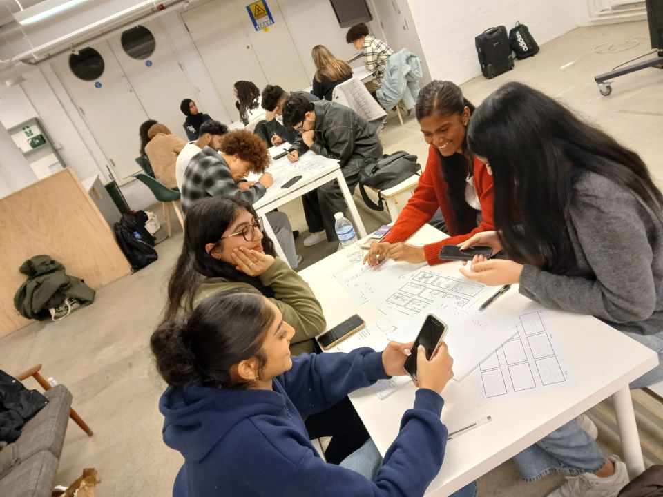 Groups of students working together at different tables in a workshop area