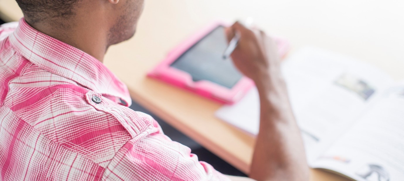 Person sat at desk with a tablet and paperwork, preparing to write