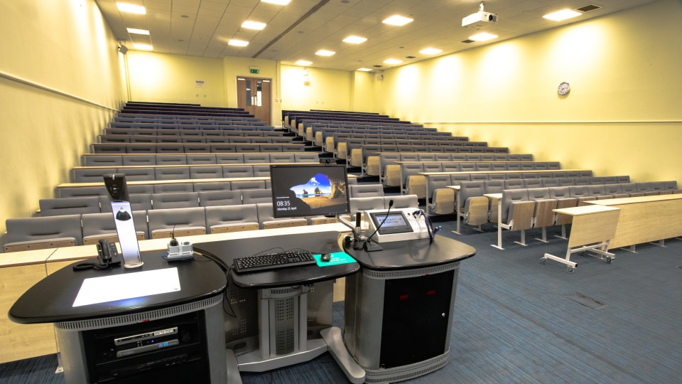 James France CC012 - Lecture hall with tiered seating, projector, and teaching podium equipped with computer and microphone.