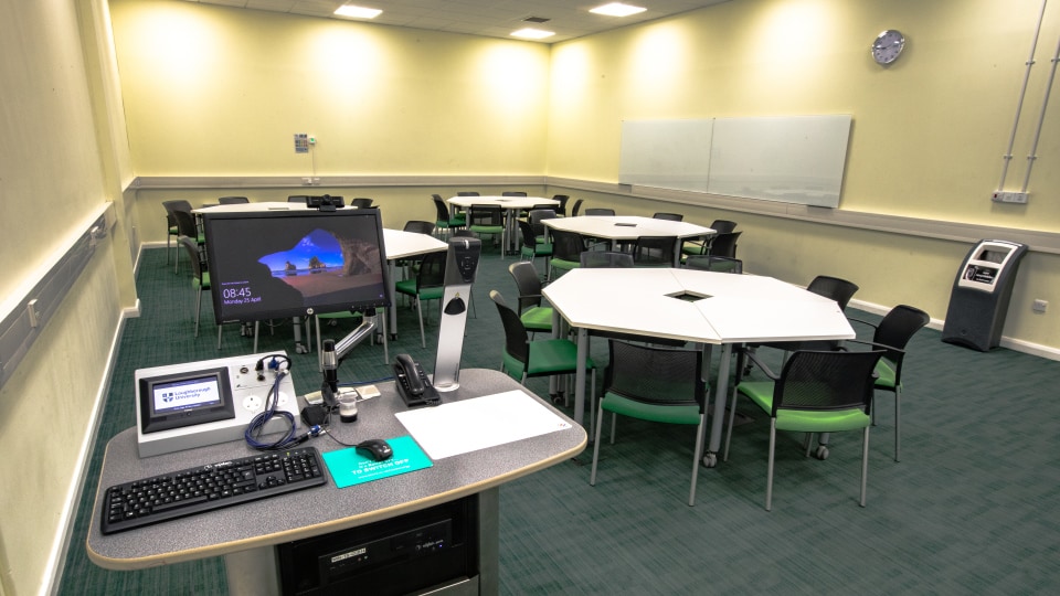James France CC014 - Teaching room with hexagonal tables, green chairs, a lectern with computer, and a wall-mounted whiteboard.