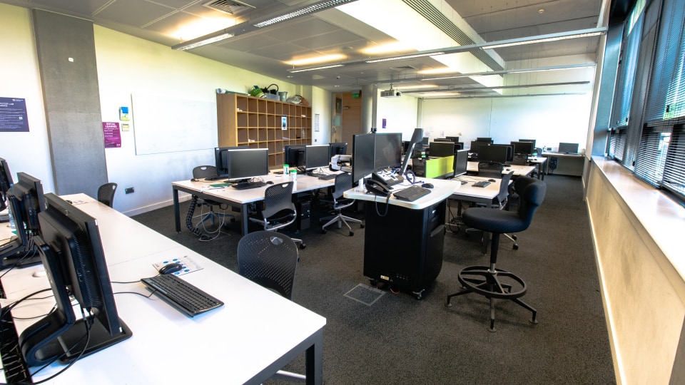 Design School LDS003 - Computer lab with multiple workstations, monitors, and chairs. Bright lighting, large windows, and a whiteboard on the wall.