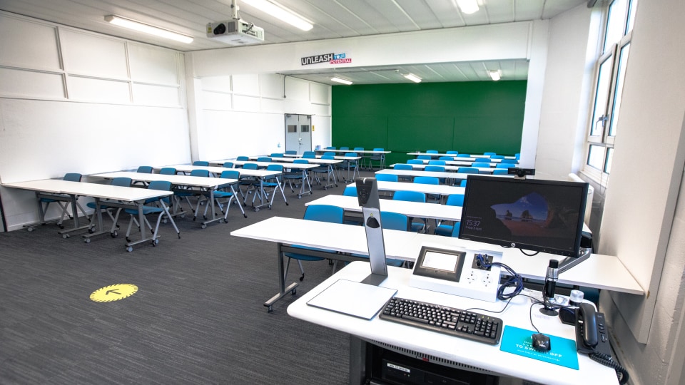 Matthew Arnold MAR106 - Teaching room with rows of desks and chairs, a computer station at the front, and a green accent wall.