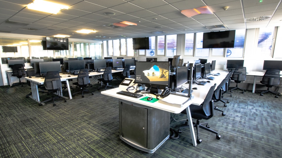 Haslegrave N005 - Modern computer lab with rows of desks, monitors, swivel chairs, and large windows. Multiple wall-mounted screens visible.