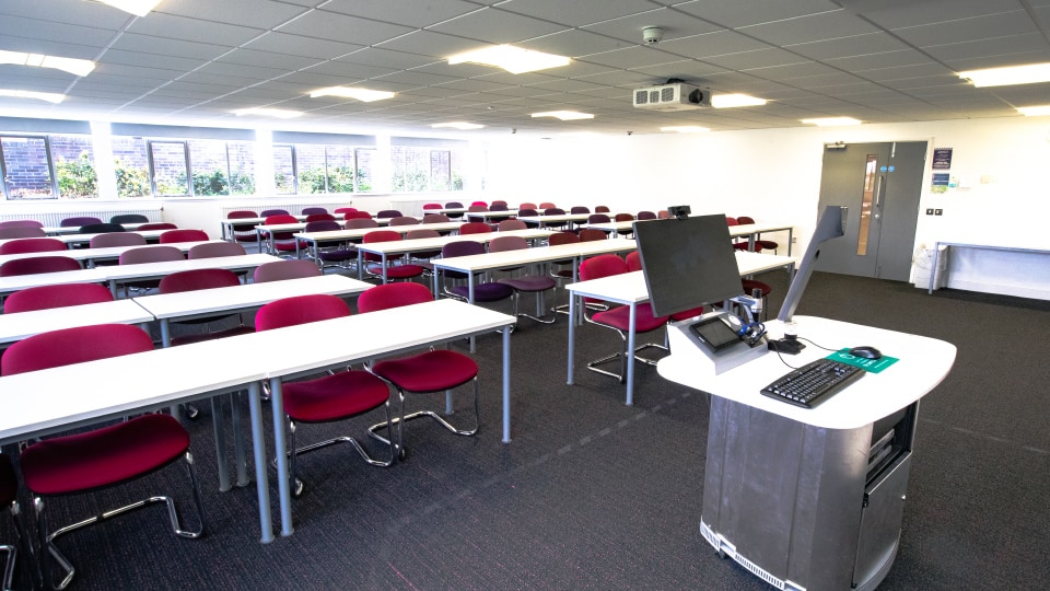 Brockington extension U006 - Teaching room with flat layout, desks in rows, projector screen at front, and ceiling lighting.