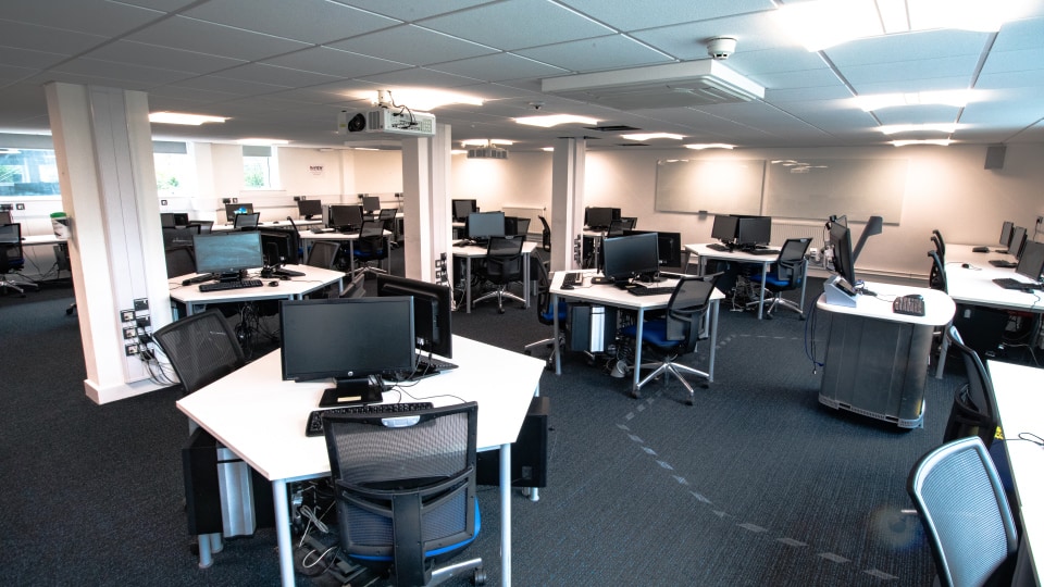 Brockington extension U007 - Computer lab with flat layout, rows of desks with monitors, projector screen at front, and ceiling lighting.