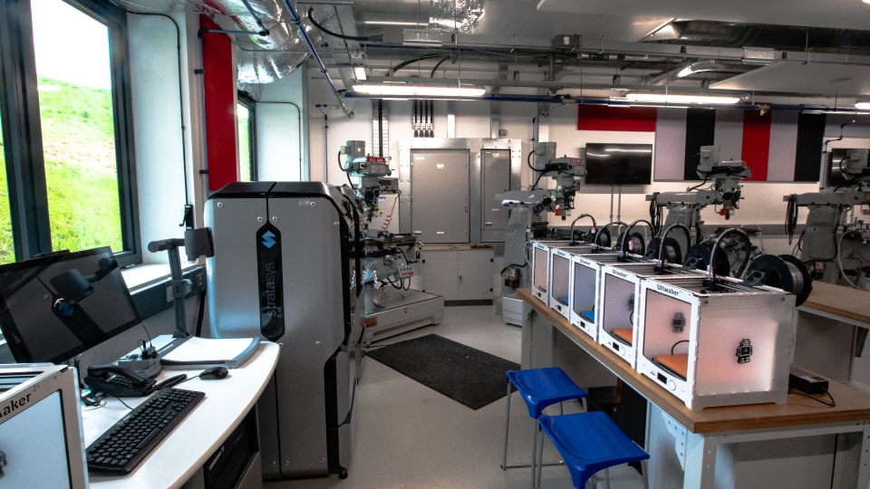 West Park Labs WPL004 - Specialist lab with 3D printers, computer workstations, and industrial machinery. Bright lighting, modern equipment, and colourful wall panels.