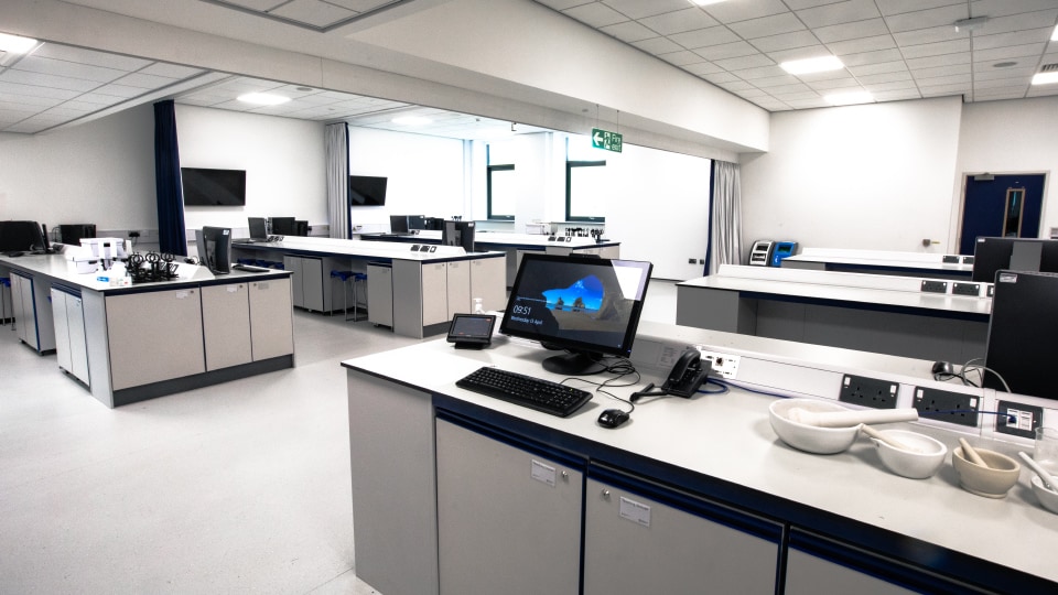 West Park Labs WPL103 - Spacious specialist lab with multiple workstations, computers, and equipment. Bright lighting, white walls, and ceiling. Monitors display screensaver.