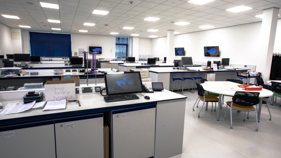 West Park Labs WPL104 - Spacious specialist lab with multiple workstations, monitors, and round tables. Bright lighting and blue blinds enhance the modern design.