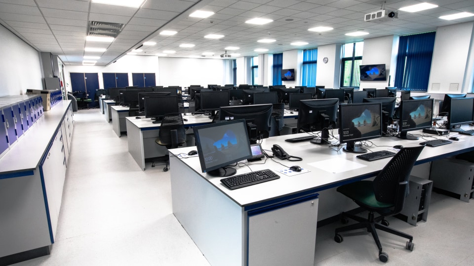 West Park Labs WPL107 - Spacious specialist lab with rows of desks, each equipped with monitors, keyboards, and chairs. Blue blinds cover large windows.