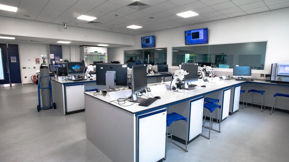 West Park Labs WPL110 - Modern specialist lab with microscopes, computers, and blue stools. Wall-mounted screens display data. Bright, spacious environment.