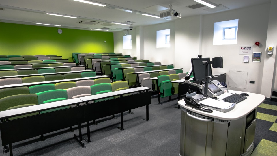 West Park Teaching Hub WPT004 - Lecture theatre with tiered seating in green and gray, a podium with computer and phone, and a bright green wall.