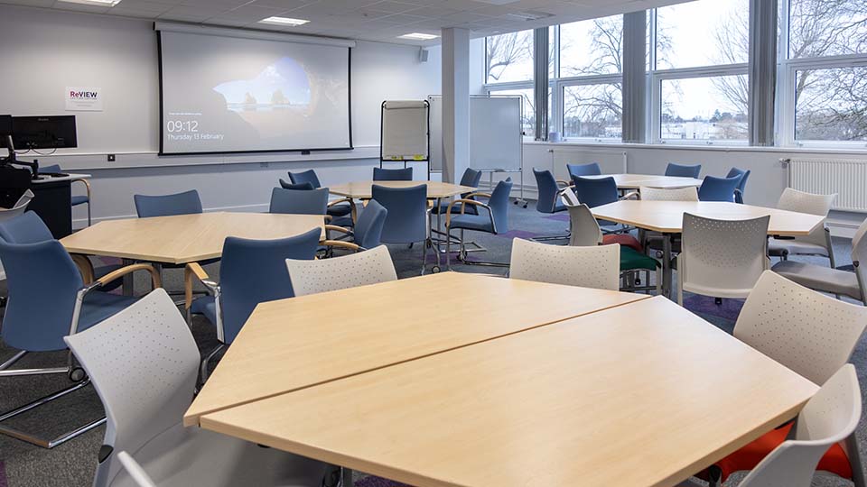 B008-teaching-room - Teaching room with flat layout, grouped desks, projector screen and bright lighting.