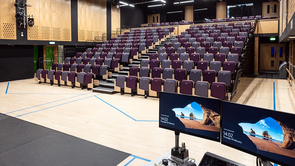 Martin Hall MHL001 - Large lecture theatre with tiered seating, wooden floor, and a teaching podium equipped with a computer and microphone.