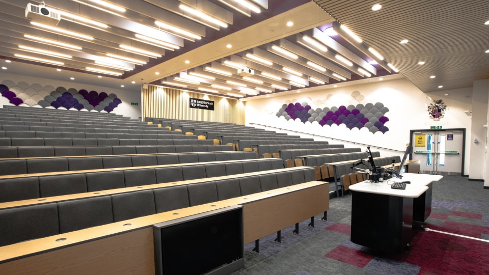 Edward Herbert EHB110b - Modern lecture hall with tiered seating, projector, and podium. Wall features geometric patterns. Sign reads 