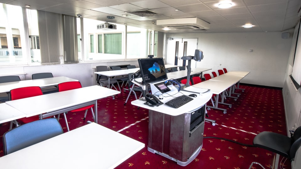 Edward Herbert EHB202 - Modern teaching room with red carpet, white tables, red and gray chairs, and a podium with computer equipment.