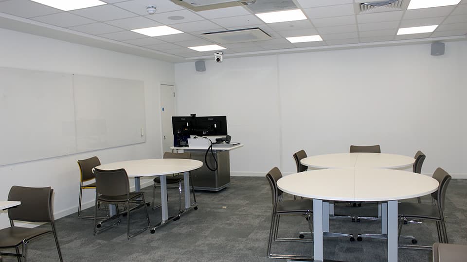 Smaller white-walled teaching space with round white tables and 2-3 chairs per table.