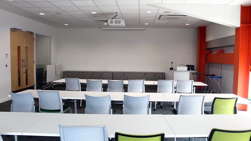 White walled smaller teaching room shown with rows of white desks.