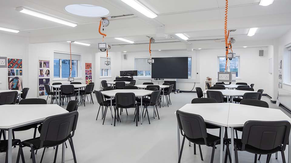 Teaching Room MHL110 - Modern teaching room with hexagonal tables, black chairs, overhead projectors, and a large screen at the front.