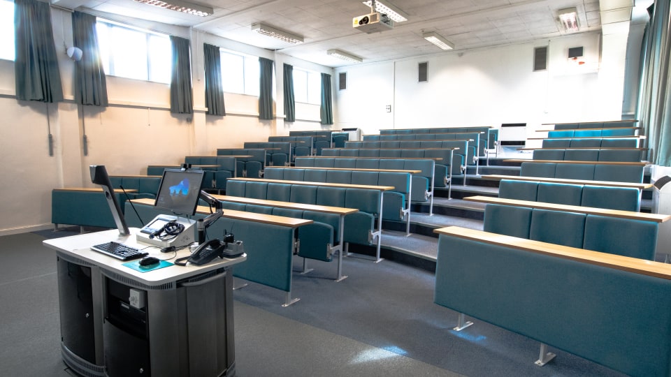Schofield SCH001 - Lecture theatre with tiered seating, projector, and a lectern equipped with a computer and phone.