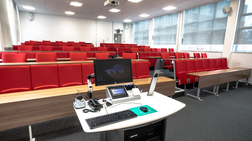Schofield SCH101 - Lecture theatre with red tiered seating, large windows, and a lectern equipped with a computer and microphone.