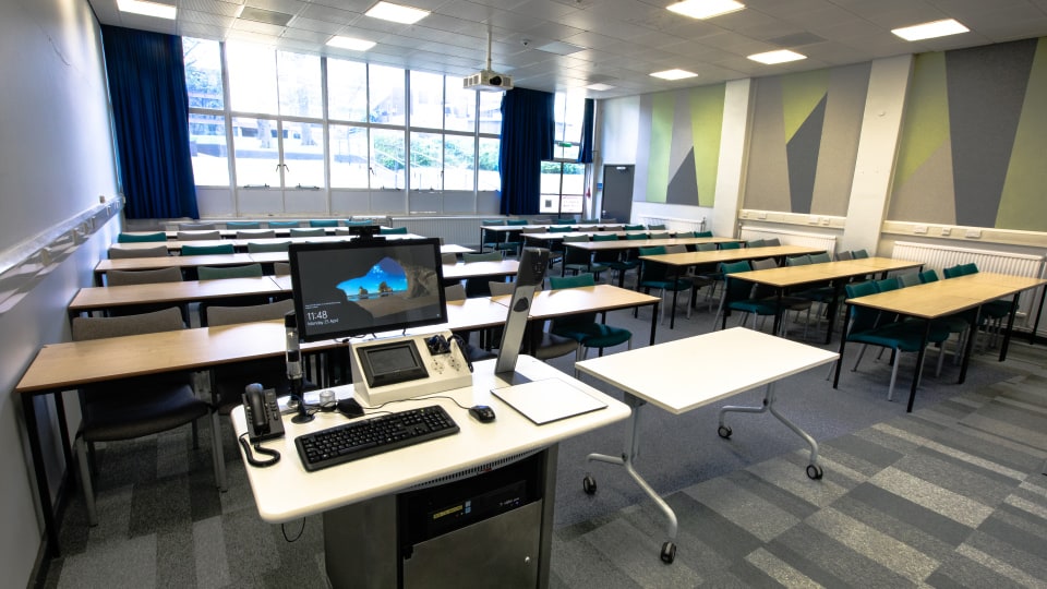 Wavy Top WAV036 - Teaching room with rows of desks and chairs, instructor's podium with computer, projector, large windows, and geometric wall design.