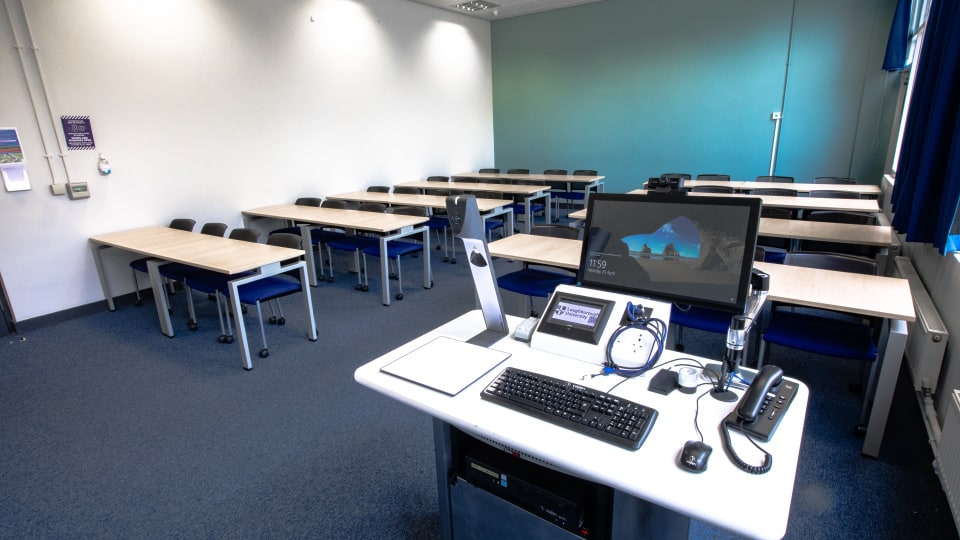 Wavy Top WAV040 - Teaching room with rows of tables and chairs, equipped with a computer station, keyboard, phone, and projector control panel.