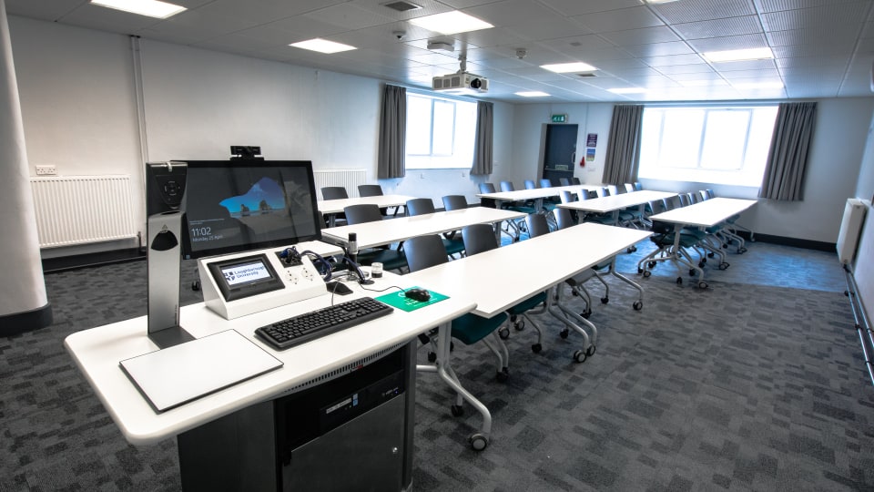 Wavy Top WAV057 - Modern teaching room with white tables, gray chairs, and a technology podium featuring a computer and control panel.